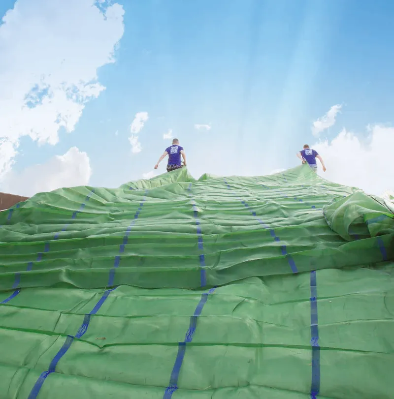 Zwei Arbeiter verlegen Silofolie auf einem Fahrsilo